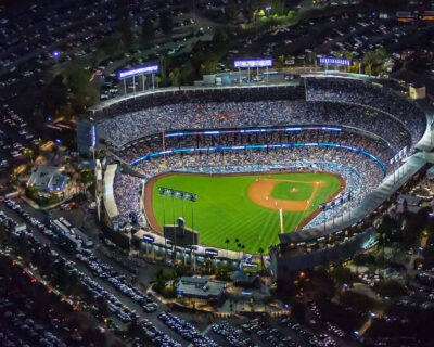 Nighttime aerial view of a stadium filled with spectators surrounded by a large parking area during a World Series game, highlighting World Series Travel Package Rates.