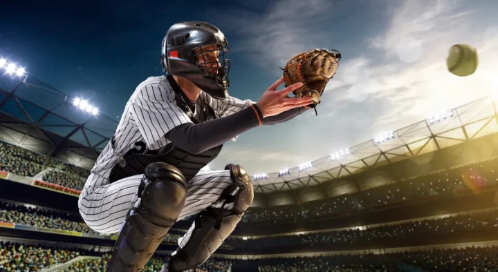 A baseball catcher in striped uniform is crouched, glove out, ready to catch a pitch in a stadium, ideal for those looking into baseball travel and ticket packages.