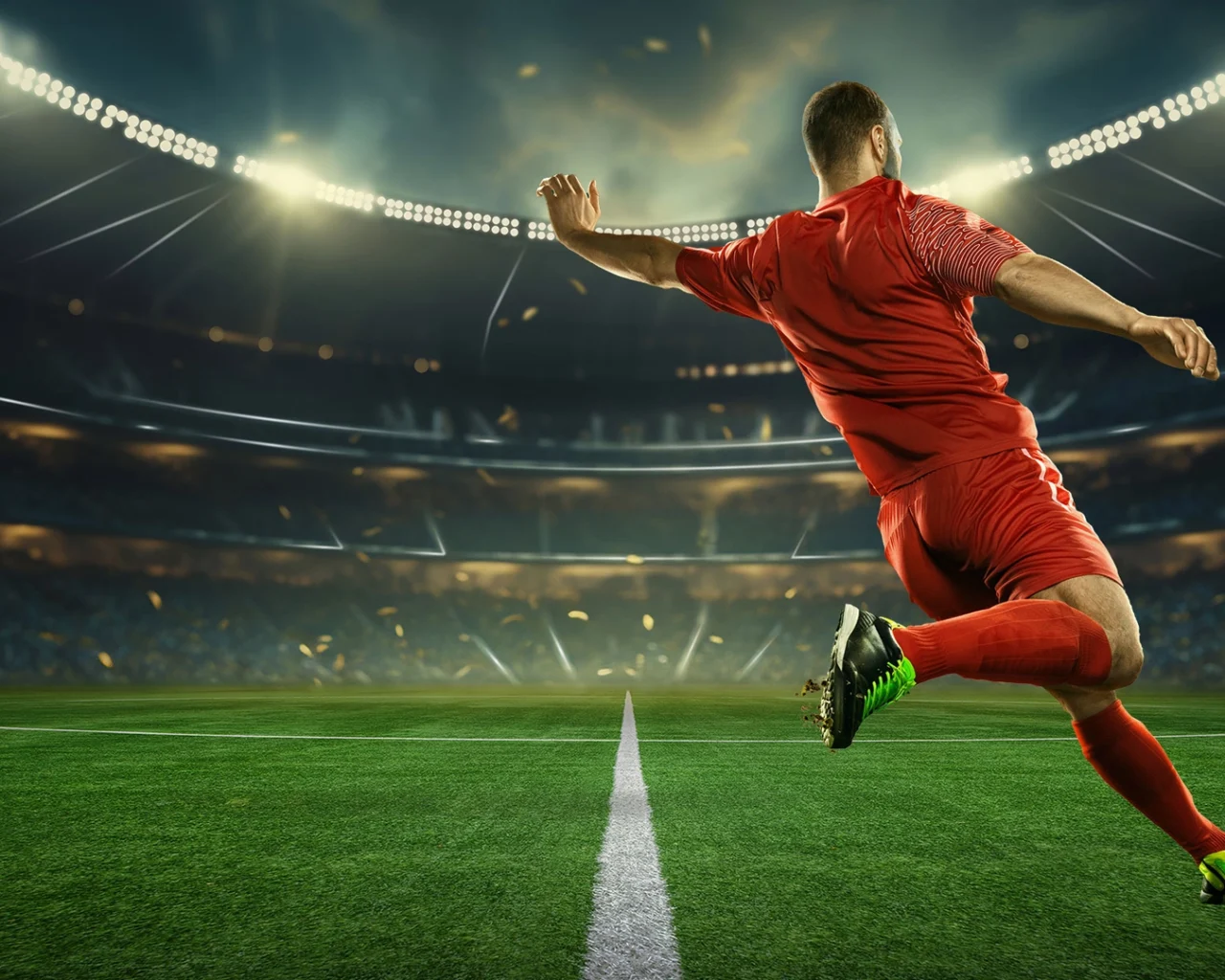 A soccer player in a red uniform kicks a ball on a brightly-lit stadium pitch, promoting sports travel packages by Roadtrips, a leader in luxury sports travel.