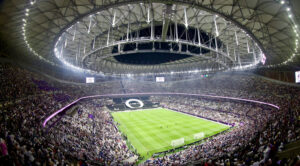 Wide-angle view of a packed stadium during a World Cup soccer match, featuring a large crowd and a closed retractable roof, in USA, Mexico, or Canada.