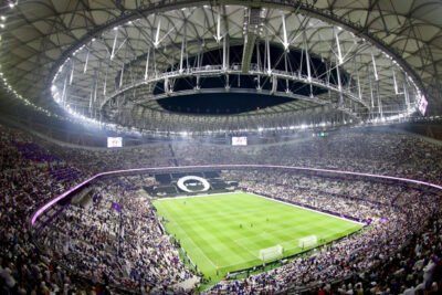Wide-angle view of a packed stadium during a World Cup soccer match, featuring a large crowd and a closed retractable roof, in USA, Mexico, or Canada.