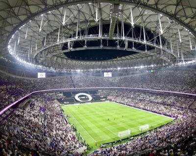 Wide-angle view of a packed stadium during a World Cup soccer match, featuring a large crowd and a closed retractable roof, in USA, Mexico, or Canada.