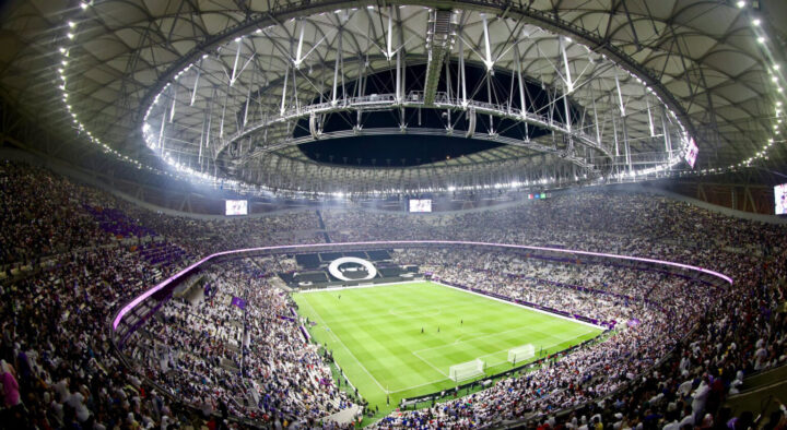 Wide-angle view of a packed stadium during a World Cup soccer match, featuring a large crowd and a closed retractable roof, in USA, Mexico, or Canada.