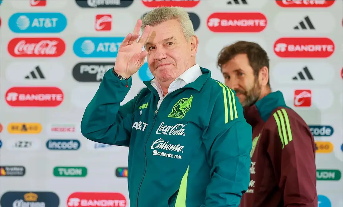 Javier Aguirre, dressed in Team Mexico gear, gestures playfully during a press conference, set against a backdrop of sponsor logos, emphasizing his leadership as fans look forward to World Cup Follow Your Team packages.