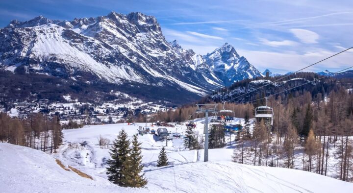 Snow-covered slopes and chairlifts with a mountain backdrop showcase a Winter Games venue in Milan and Cortina.