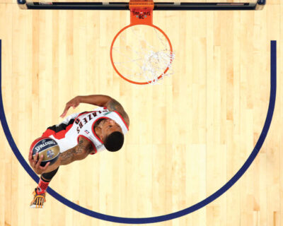 Top-down view of a basketball player in a white and red uniform scoring a basket, capturing the excitement ideal for basketball travel and hotel packages.