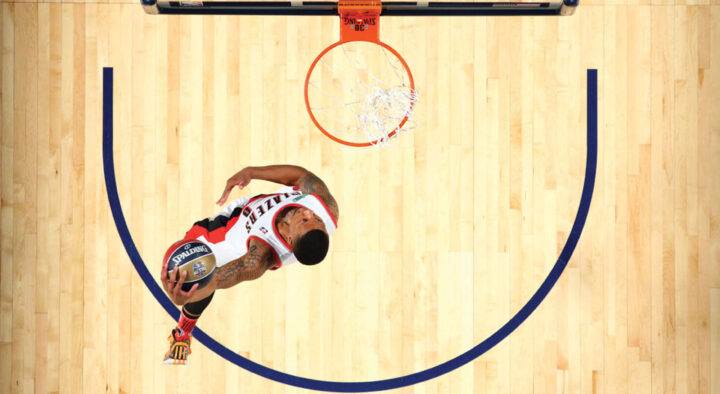 Top-down view of a basketball player in a white and red uniform scoring a basket, capturing the excitement ideal for basketball travel and hotel packages.