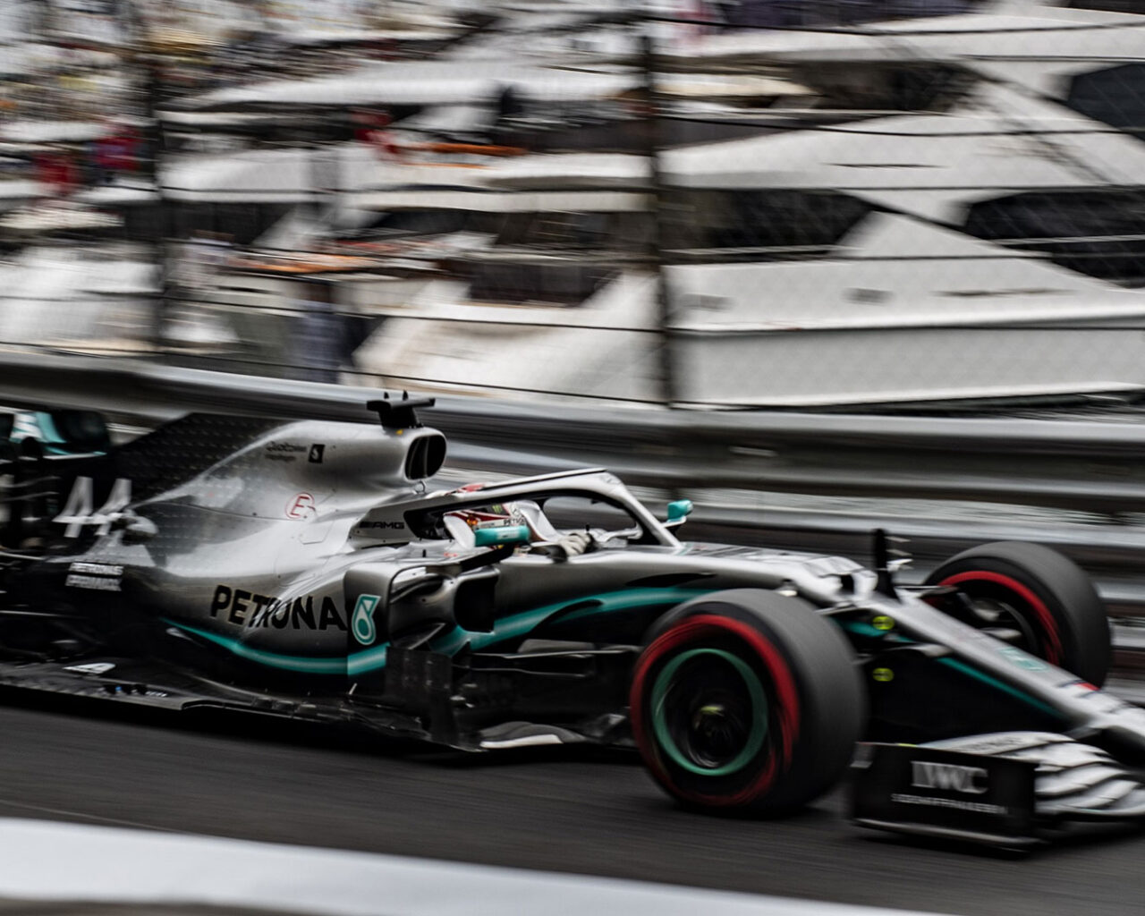 A Formula One car speeds along a track with blurred yachts in the background, highlighting the excitement of auto racing at prestigious events like the Grand Prix.