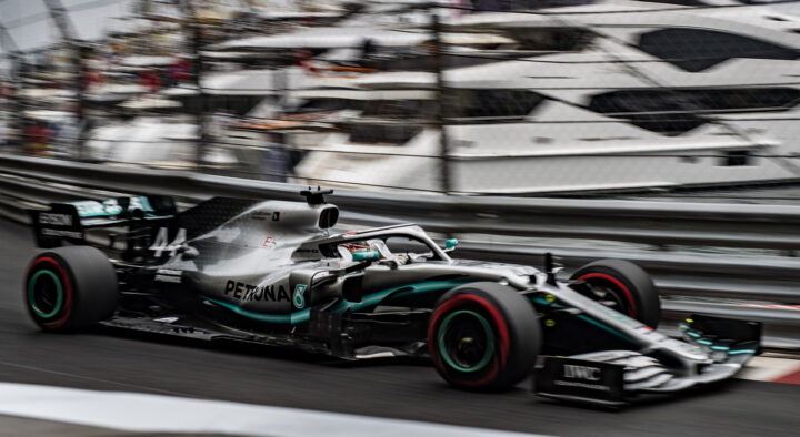 A Formula One car speeds along a track with blurred yachts in the background, highlighting the excitement of auto racing at prestigious events like the Grand Prix.
