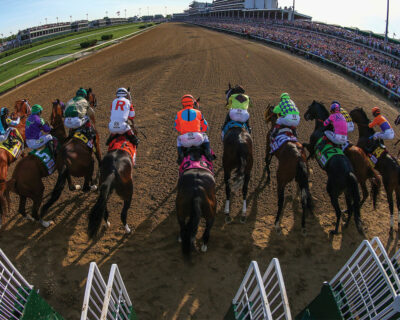 Horse racing event in full swing with jockeys on horses in colorful attire, racing on a dirt track in front of a packed grandstand, perfect for horse racing travel packages.