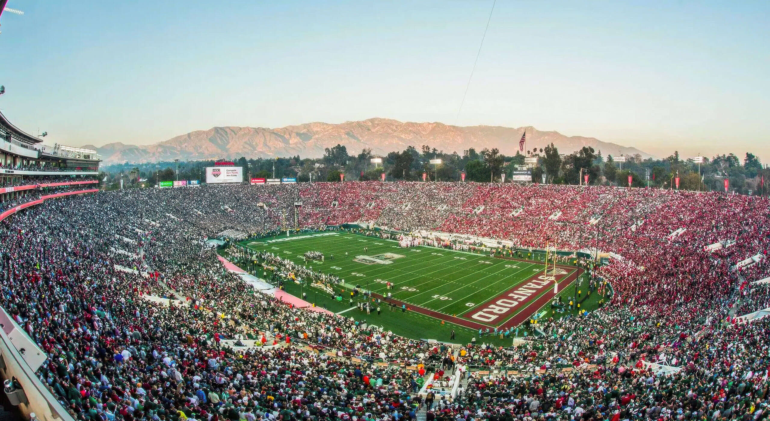 A panoramic view of a packed stadium during a football game, set against a backdrop of mountains, ideal for those seeking football travel packages that include hotel and ticket options.