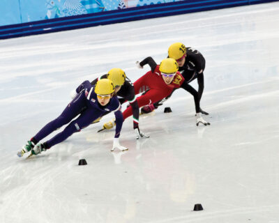 Speed skaters compete intensely on an ice track, captured in vivid detail, perfect for those interested in Winter Games Travel Packages and Tours.