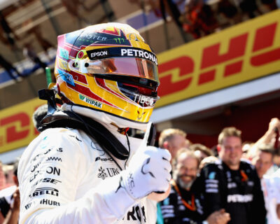 Race car driver in white suit and vibrant helmet celebrates with team members at the Spanish Grand Prix, reflecting a moment of joy and triumph in motorsports.