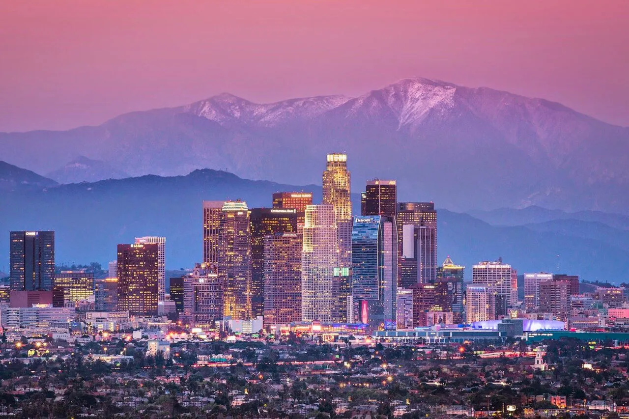Downtown Los Angeles skyline during sunset with illuminated buildings and distant mountains, providing a backdrop for the Summer Games Los Angeles Area Map.