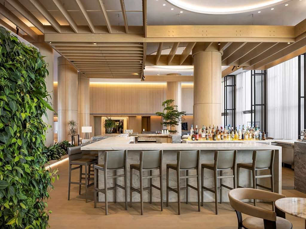 Modern bar lounge at the Fairmont Century Plaza in Los Angeles, featuring a sleek bar counter and lush greenery, ideal for Summer Games accommodations.