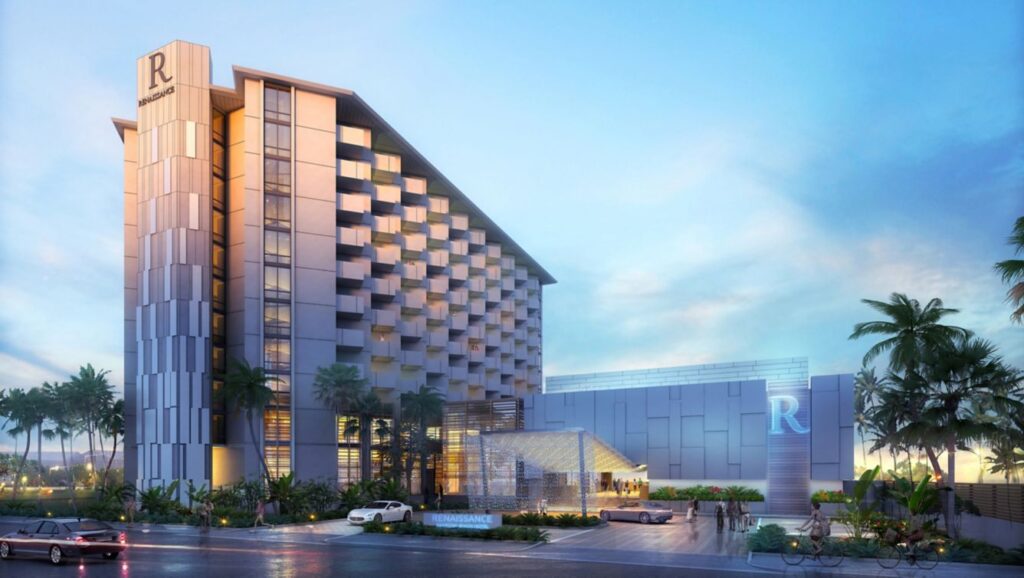 Twilight view of the Renaissance Daytona Beach Oceanfront Hotel, featuring a modern design with a lit facade, palm trees, and vehicles passing by on North Atlantic Avenue in Daytona Beach, Florida.