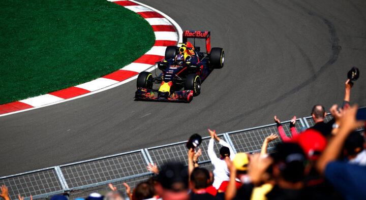 Racing car speeding around a track corner, closely watched by cheering fans, symbolizing the excitement of the Canadian Grand Prix.