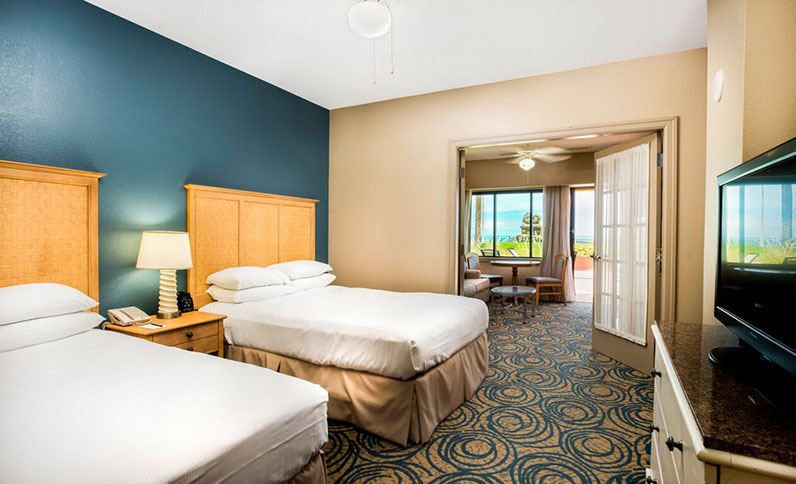 Hotel room at Hilton Daytona Beach Oceanfront Resort, featuring two beds, a desk area, and open French doors leading to a view of the ocean; ideal accommodation for Daytona 500 visitors.