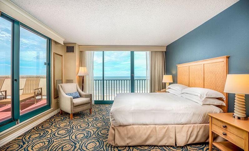 Luxury hotel room at Hilton Daytona Beach Oceanfront Resort, featuring a large bed and balcony view of the ocean, ideal for Daytona 500 accommodations.