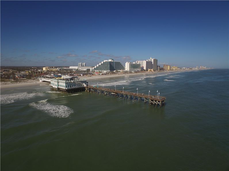 Aerial view of Daytona Beach showcasing the pier and the Hilton Daytona Beach Oceanfront Resort, ideal for visitors looking for luxury accommodations near Daytona 500 events.