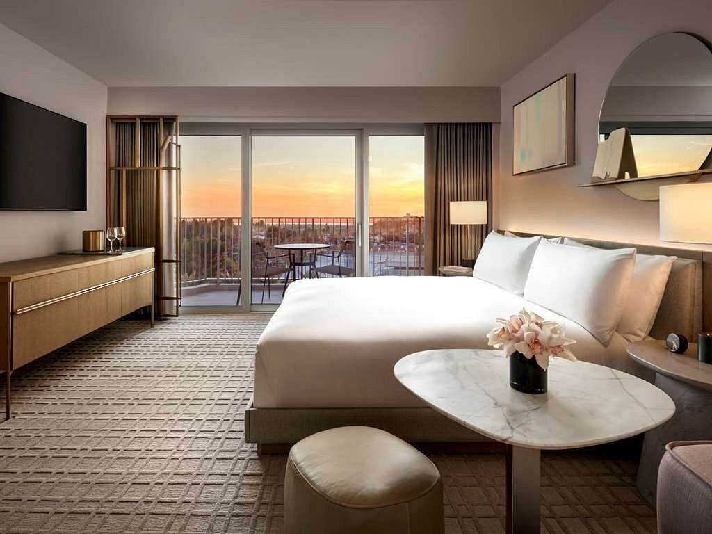 A stylish guest room at Fairmont Century Plaza in Los Angeles, featuring a king-sized bed, elegant furniture, and a sunset view from the balcony. Ideal accommodation for the Summer Games events.