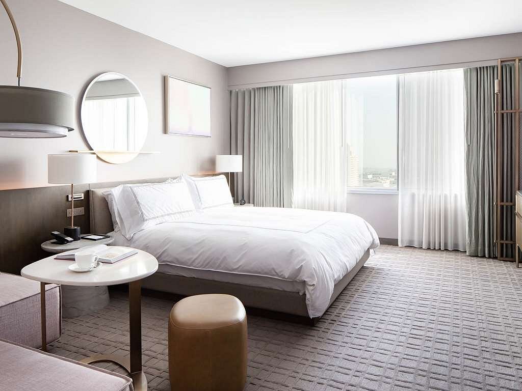 Modern hotel room at Fairmont Century Plaza, featuring a large bed, minimalist decor, and a city view, ideal for guests attending the Summer Games in Los Angeles.