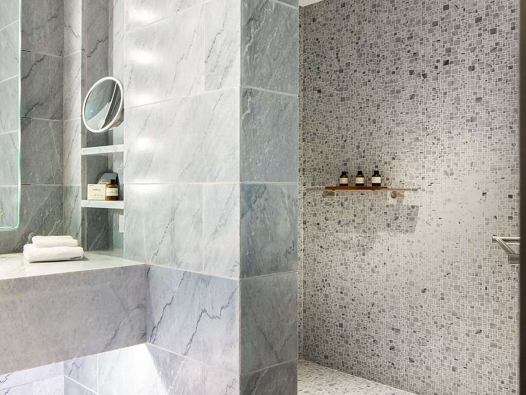 Modern marble bathroom at the Fairmont Century Plaza, featuring a wall of gray textured tiles on one side and mosaic tiles on the other.