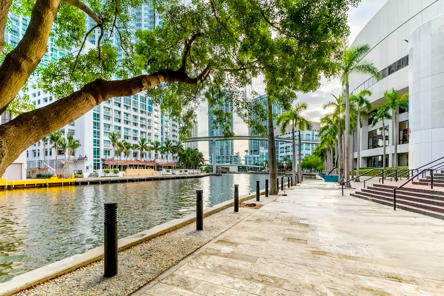 Riverside walkway at Hyatt Regency Miami, featuring a serene view with lush trees, modern buildings, and a calm waterfront, ideal for guests attending Miami Grand Prix events.