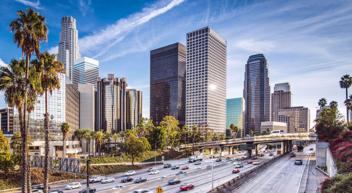 Los Angeles skyline featuring bustling traffic on a highway and palm trees, highlighting the city's preparation for the Summer Games and potential accommodations near major venues.