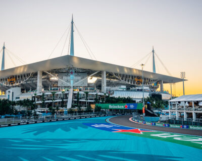 Sunrise view over a race track at the Miami Grand Prix venue with prominent Heineken branding, modern architecture, and multiple levels of spectator areas.