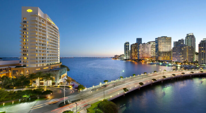 Twilight view of a busy road beside an ocean, highlighting Miami hotels and modern architecture, ideal for visitors planning to attend the Miami Grand Prix.