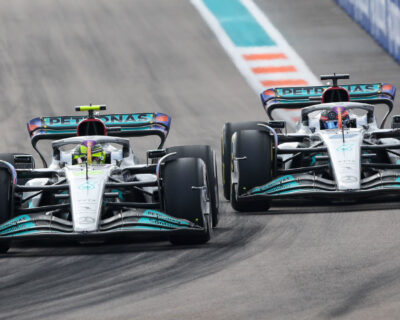 Two Formula One cars from the Petronas team race closely on a track, capturing the excitement of Grand Prix auto racing at events like Daytona and Indianapolis.