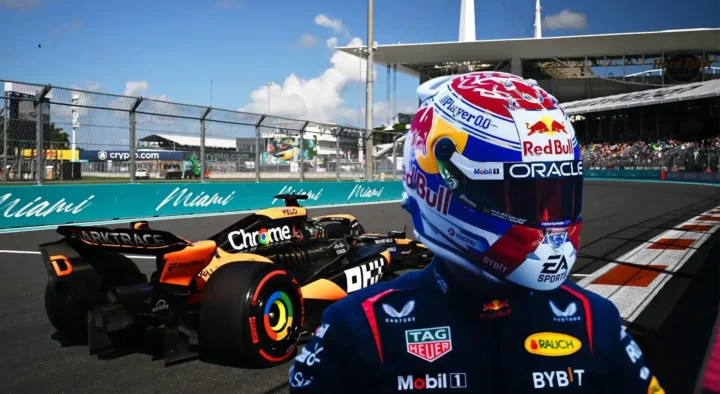 A helmeted race car driver faces a colorful Formula 1 car at the Miami International Autodrome, emphasizing action-packed auto racing travel packages in Miami, FL.