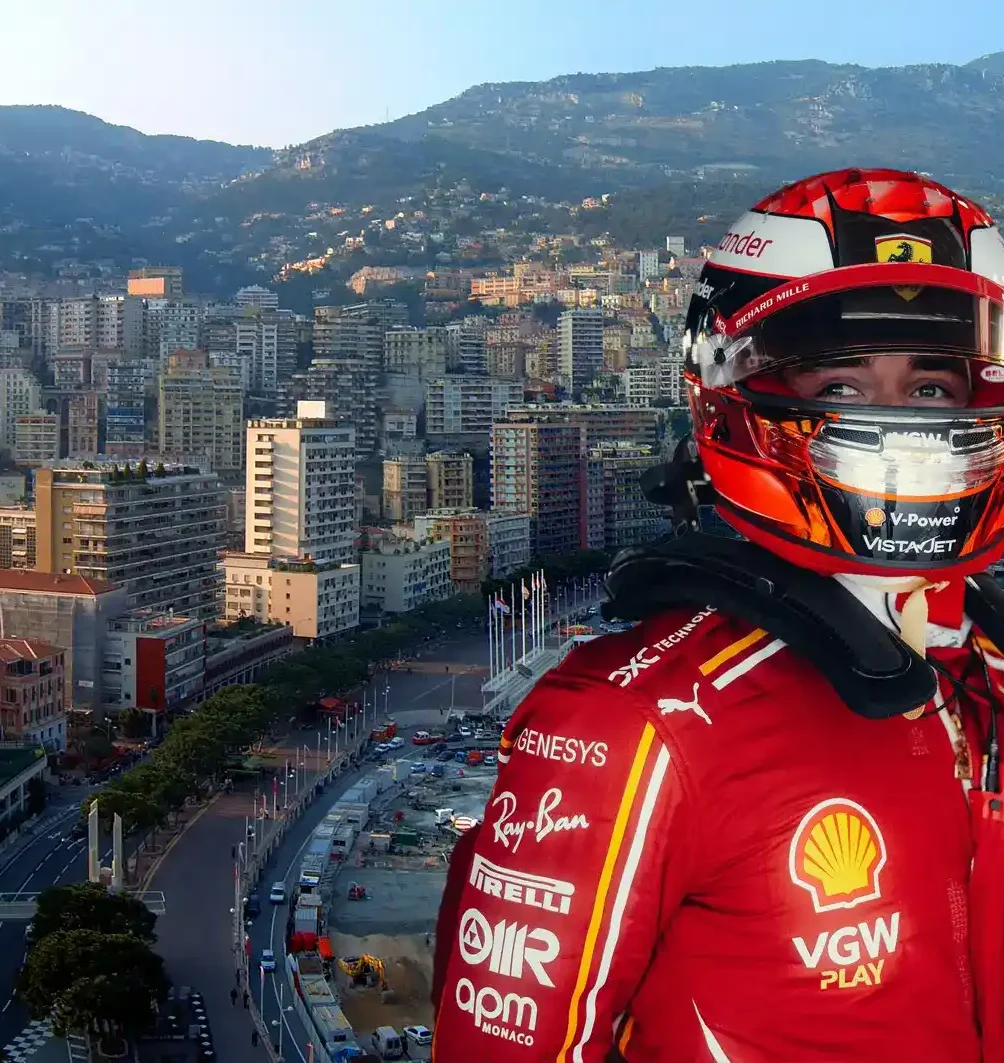 Race car driver in a red racing suit looks out towards the scenic Monaco harbor and cityscape, highlighting the luxury and excitement of the Monaco Grand Prix Packages.