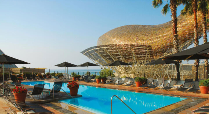 Luxury hotel pool area in Barcelona, featuring lounge chairs, umbrellas, and a distinctive metallic structure, perfect for guests attending the Spanish Grand Prix.