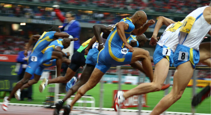 Male athletes sprint at the start of a track race at the Summer Games, capturing the intense competition and focus required in sports.