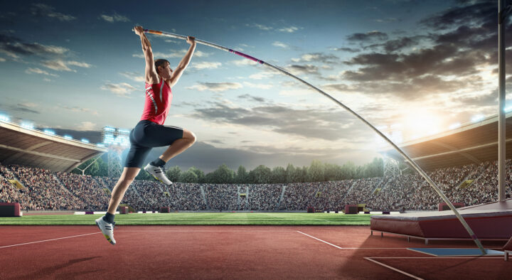 An athlete performs a pole vault at a stadium packed with spectators, likely related to the upcoming Summer Games in Los Angeles, emphasizing exciting sports action and travel opportunities.