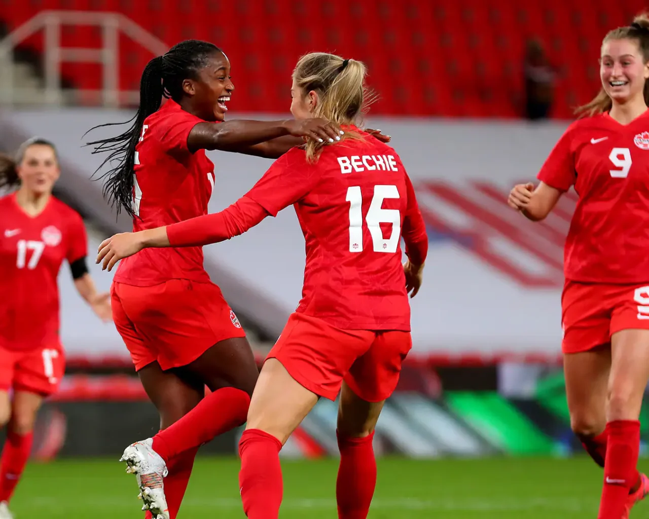 Two women in red Canada soccer uniforms celebrating on the field, embodying the thrill of international women's soccer competitions like the Women's World Cup in Brazil.