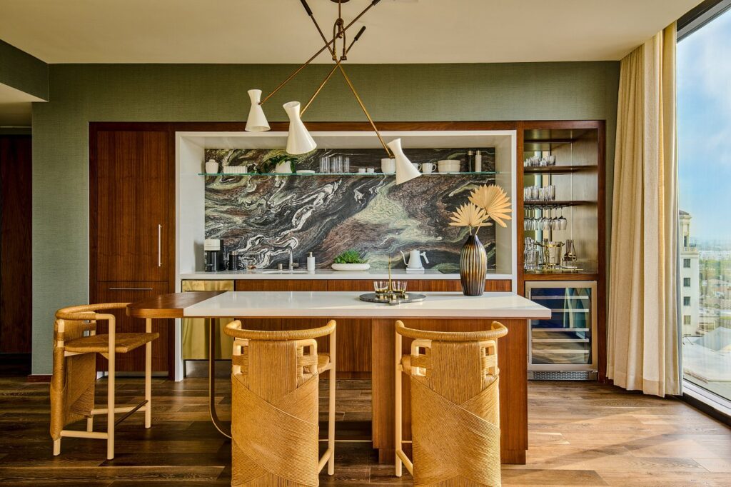 Elegant hotel kitchen area featuring modern design, wooden bar stools at a marble counter, and a striking wall art, located in Thompson Hollywood by Hyatt, Los Angeles, ideal for guests visiting for the Summer Games.