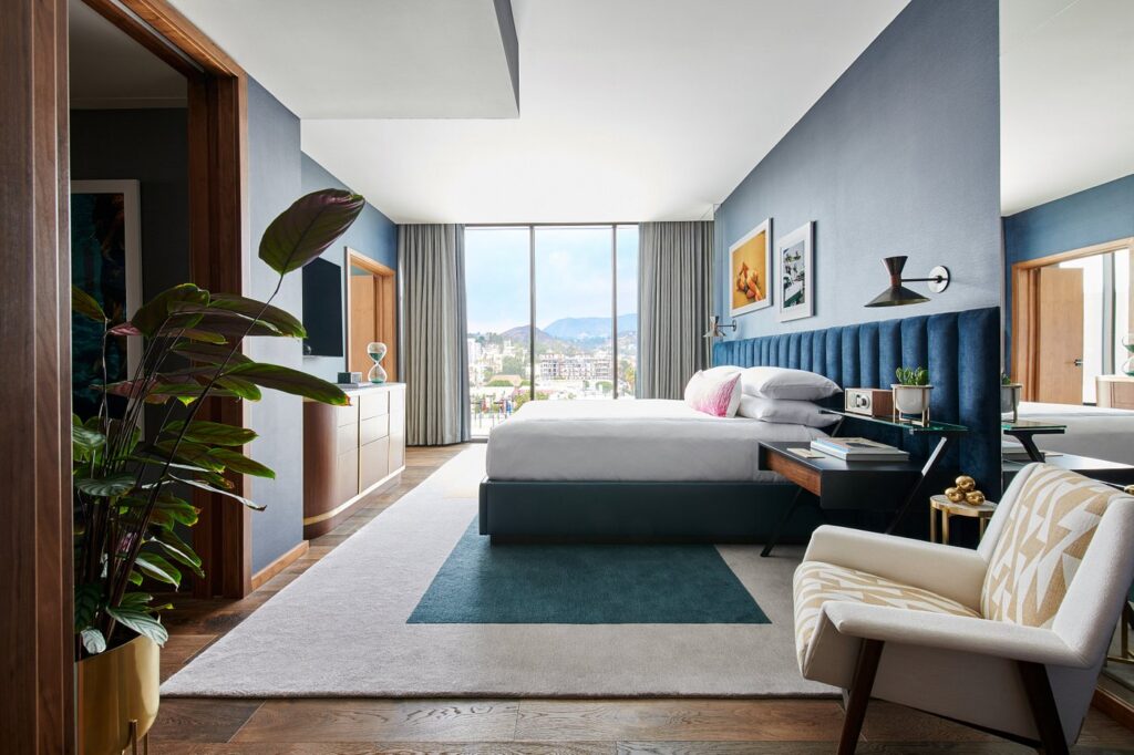 Luxurious hotel room at Thompson Hollywood by Hyatt, featuring a plush blue headboard, stylish seating area, and expansive view of Los Angeles, ideal for guests attending the Summer Games.