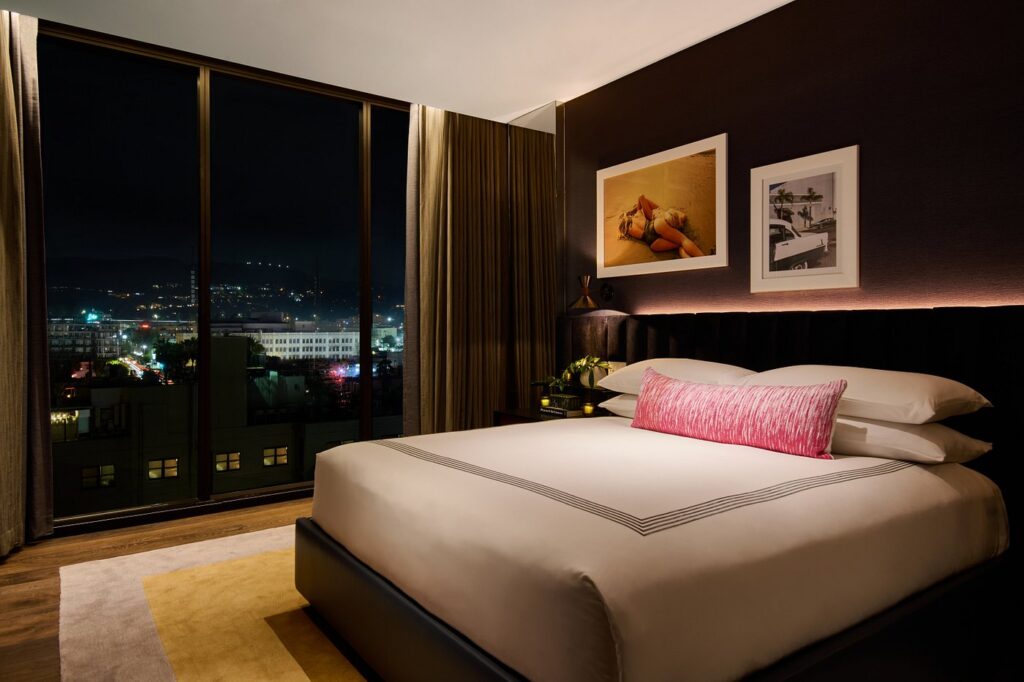 Luxury bedroom in Thompson Hollywood by Hyatt, with a king-size bed, artistic decor, and a view of Los Angeles lights, perfect for visitors looking for accommodations near the Summer Games venues.