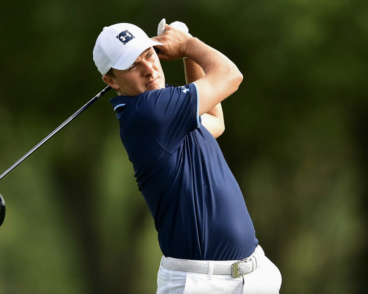 A golfer in a white cap and blue shirt swings his club during a shot at the US Open Golf Tournament, showcasing prowess central to event packages and tours.
