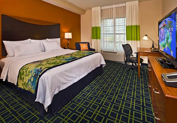 Interior of a hotel room featuring a large bed with a colorful bedspread, a desk with a chair, and a flat-screen TV.