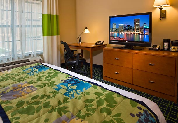 Hotel room at Fairfield Inn & Suites Baltimore with colorful bedding, a desk, office chair, and TV displaying a cityscape, ideal for Preakness Stakes accommodations.