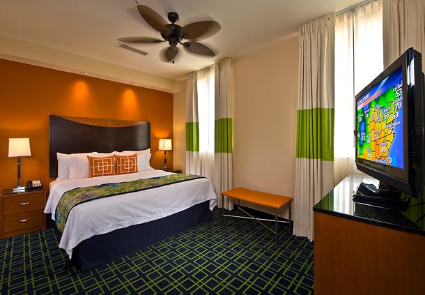 Bright and modern hotel room at Fairfield Inn & Suites Baltimore Downtown/Inner Harbor, displaying a large bed, a flat-screen TV showing a cartoon, and stylish decor. Ideal for visitors to the Preakness Stakes.