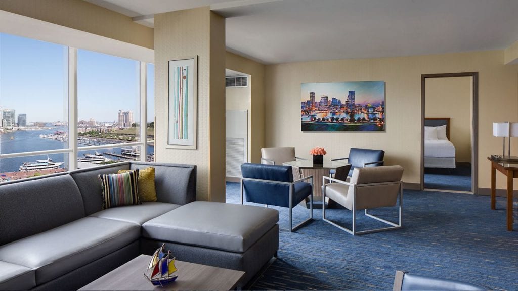 Spacious suite at Hyatt Regency Baltimore Inner Harbor with panoramic views of the harbor, modern furnishings, and a cityscape painting, ideal for visitors to the Preakness Stakes.