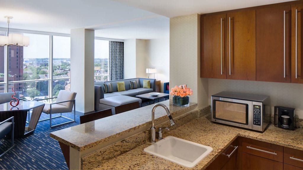 Modern suite in the Hyatt Regency Baltimore Inner Harbor showcasing a kitchen area, comfortable seating, and a city view, ideal for visitors attending the Preakness Stakes.