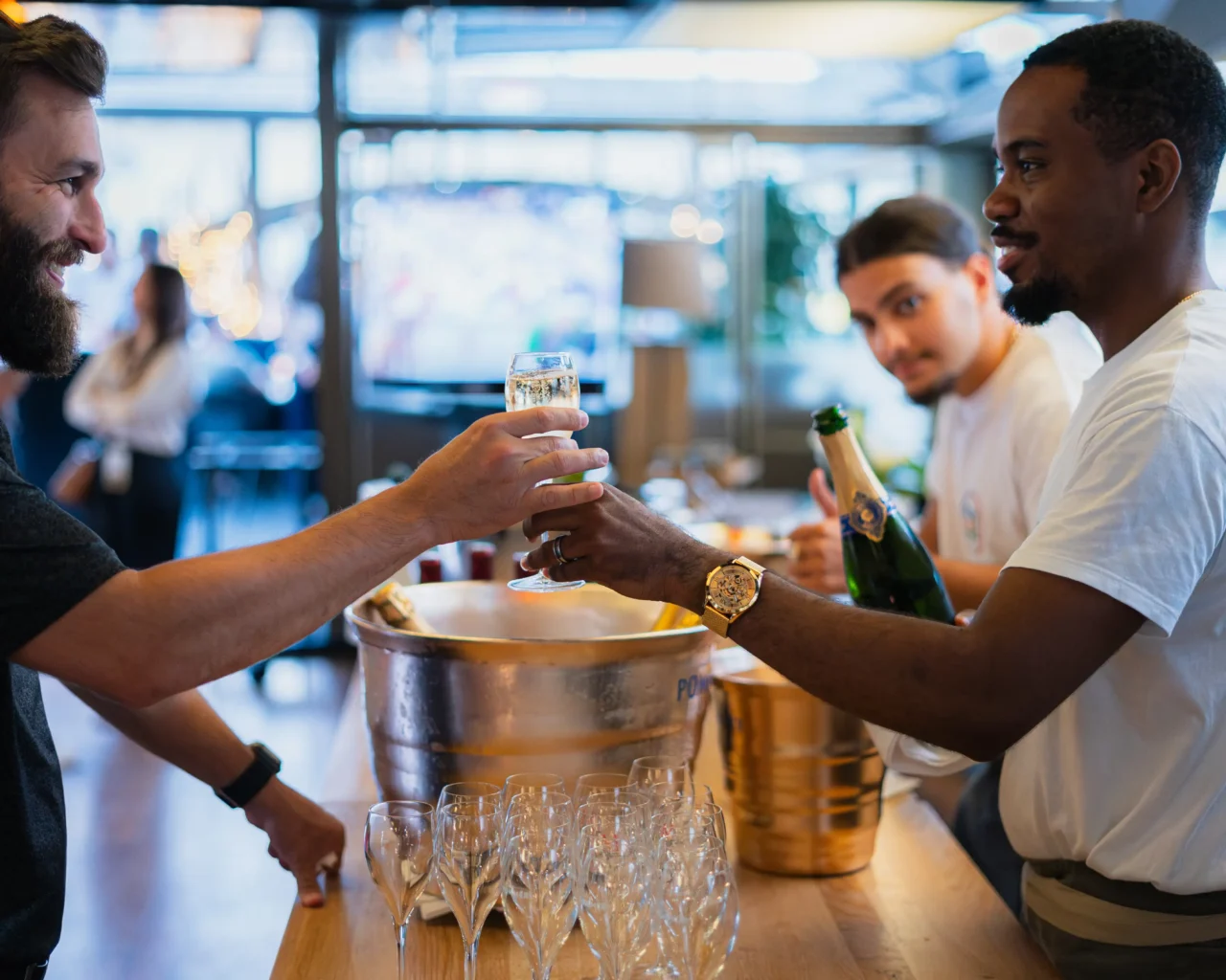 Three men clink glasses in a celebratory toast at a bar, highlighting a scene of hospitality potentially linked to Long Island, New York hotels and travel options.