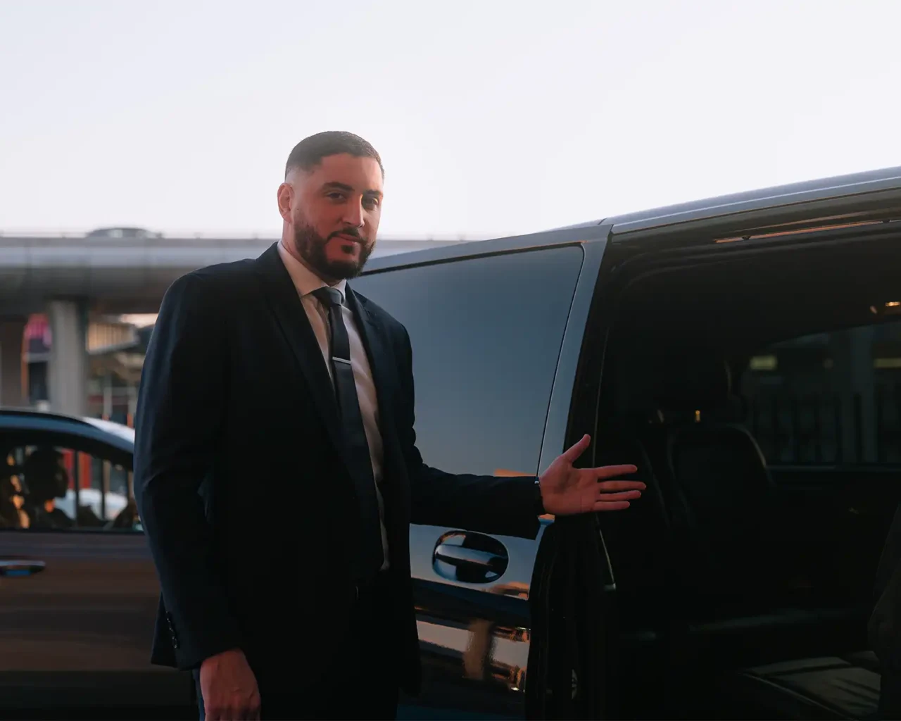 Man in a suit opens a car door at an airport, providing meet-and-greet services as part of the Andaz Munich Schwabinger Tor Preferred Seating package.