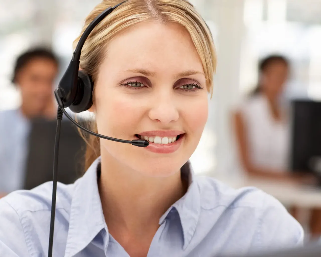 A smiling woman with a headset in an office environment, providing customer service related to travel accommodations for the Ryder Cup in Long Island, New York.